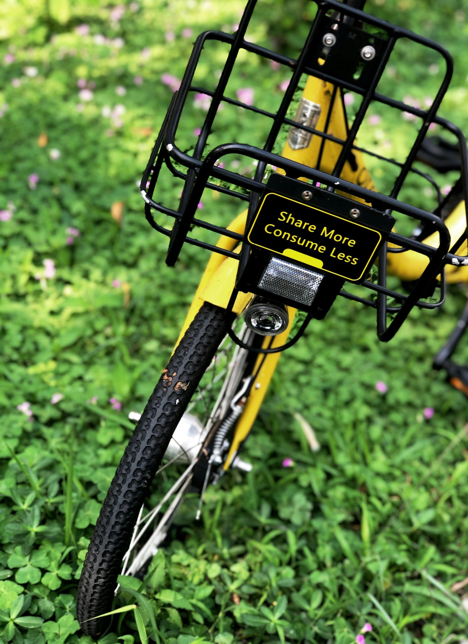 Share More Consume Less sign on a bicycle basket A Share More Consume Less sign fixed to a bicycle's front basket