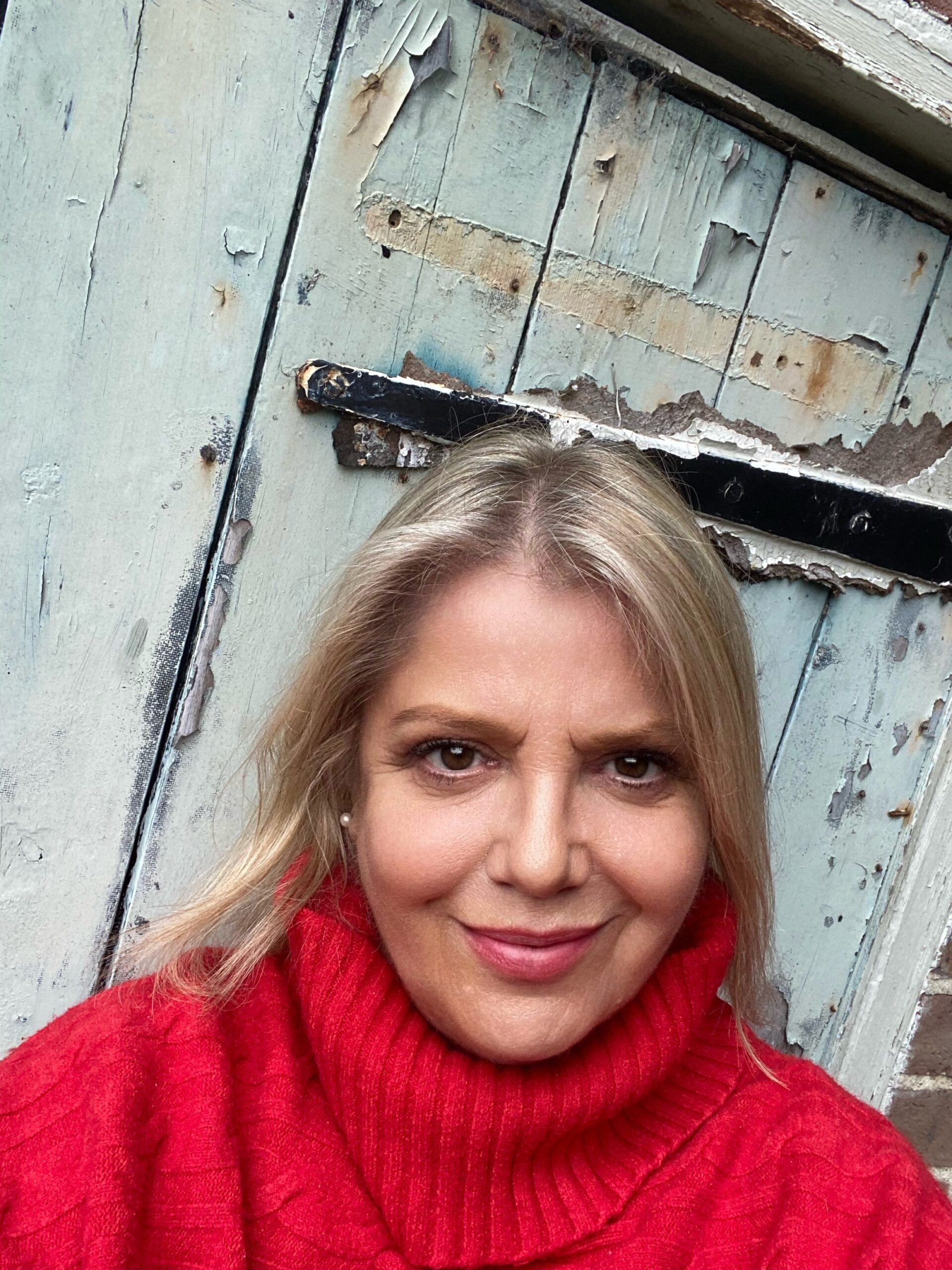 Sharon Callcut in a red jumper, smiling, against a weathered pale blue door