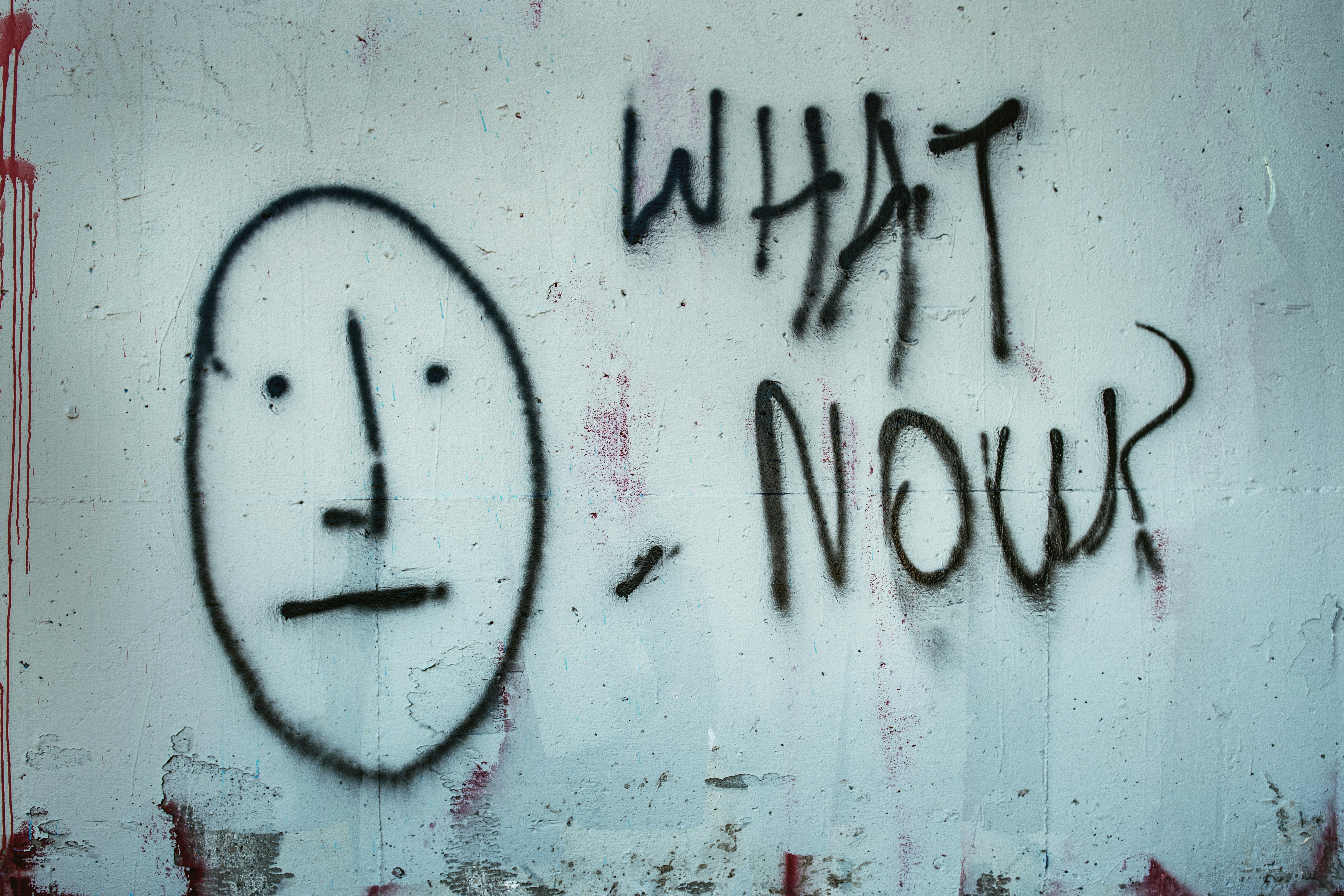 A spray-painted face and the words What Now on a wall