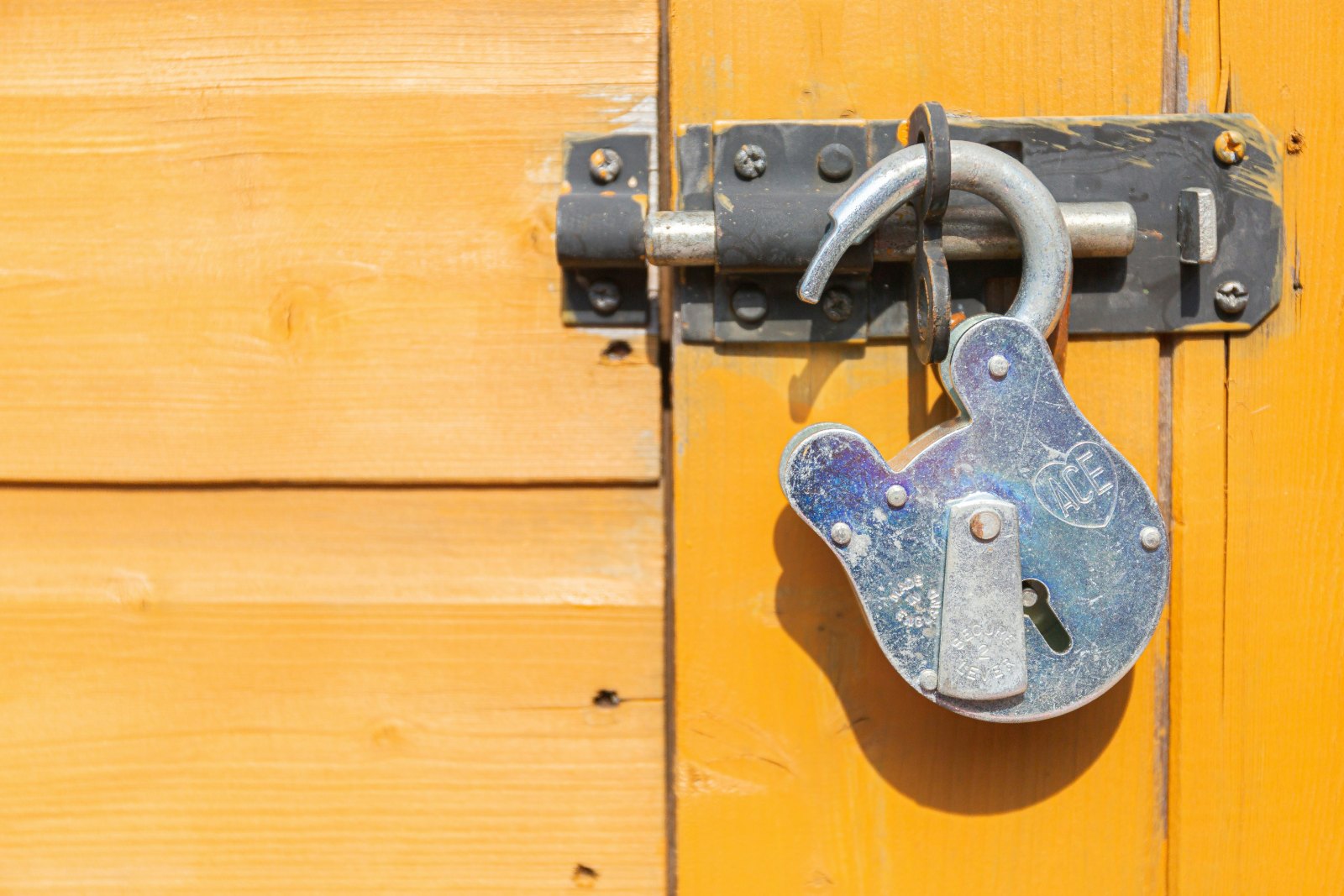 Open silver padlock hanging from a bolt on a yellow-orange wooden door