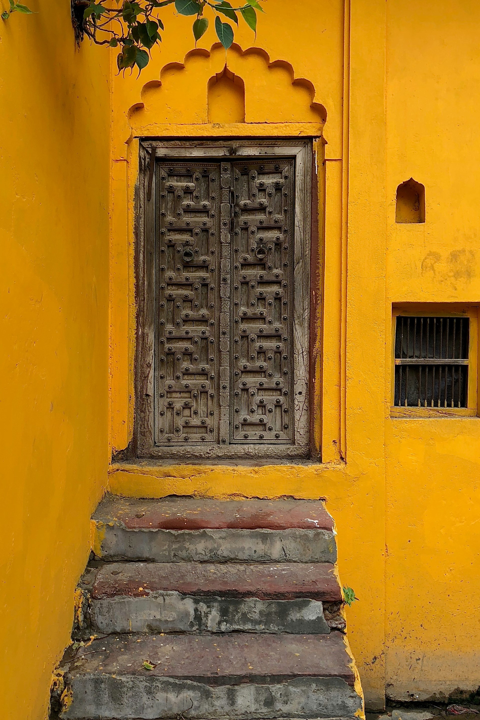 Carved wooden double door with stone steps, set into a rich ochre-yellow wall