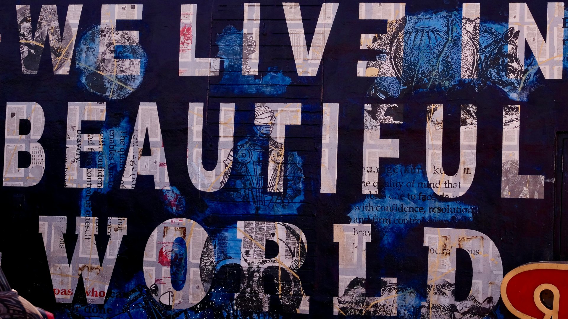 Wall artwork with the words We Live in a Beautiful World in large white collaged lettering on a dark blue background